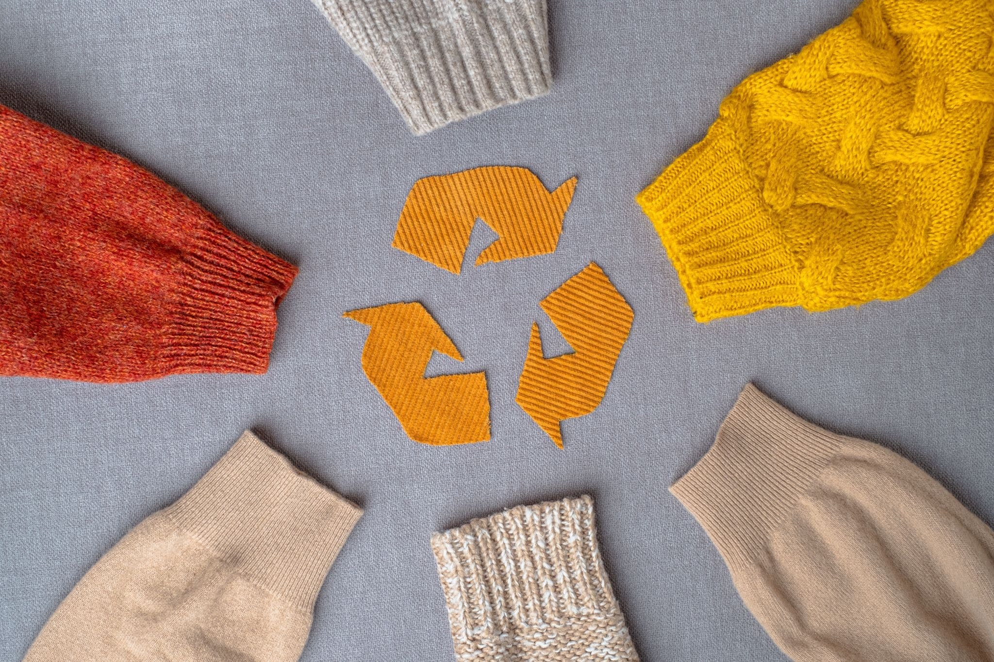 Variety of sweaters surrounding recycling symbol, illustrating sustainable fashion