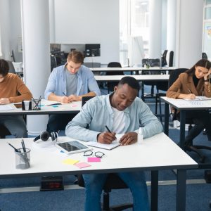 Diverse group of students sitting at desk writing in classroom